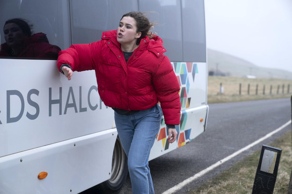  Shetland season 8, episode 1: Ellen Quinn (Maisie Norma Seaton), wearing jeans and a red puffer jacket, runs alongside a bus, banging on the side of the vehicle. 