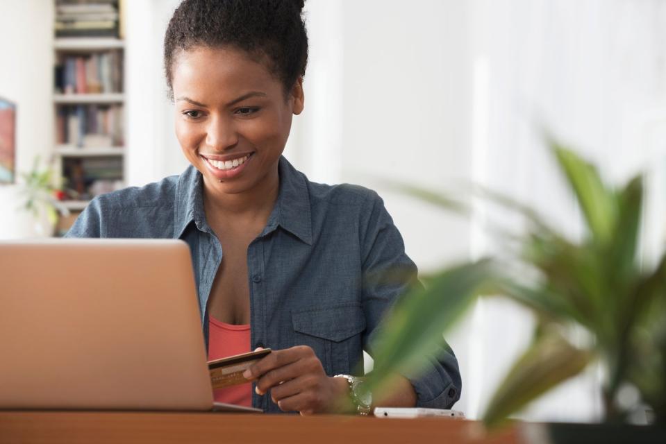 A smiling person holding a credit card in their left hand while contemplating an online purchase. 