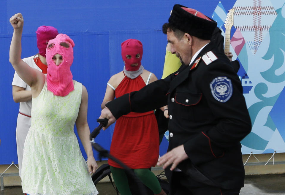 Members of the punk group Pussy Riot, including Nadezhda Tolokonnikova in the blue balaclava and Maria Alekhina in the pink balaclava, are attacked by Cossack militia in Sochi, Russia, on Wednesday, Feb. 19, 2014. The group had gathered in a downtown Sochi restaurant, about 30km (21miles) from where the Winter Olympics are being held. They ran out of the restaurant wearing brightly colored clothes and ski masks and were set upon by about a dozen Cossacks, who are used by police authorities in Russia to patrol the streets. (AP Photo/Morry Gash)