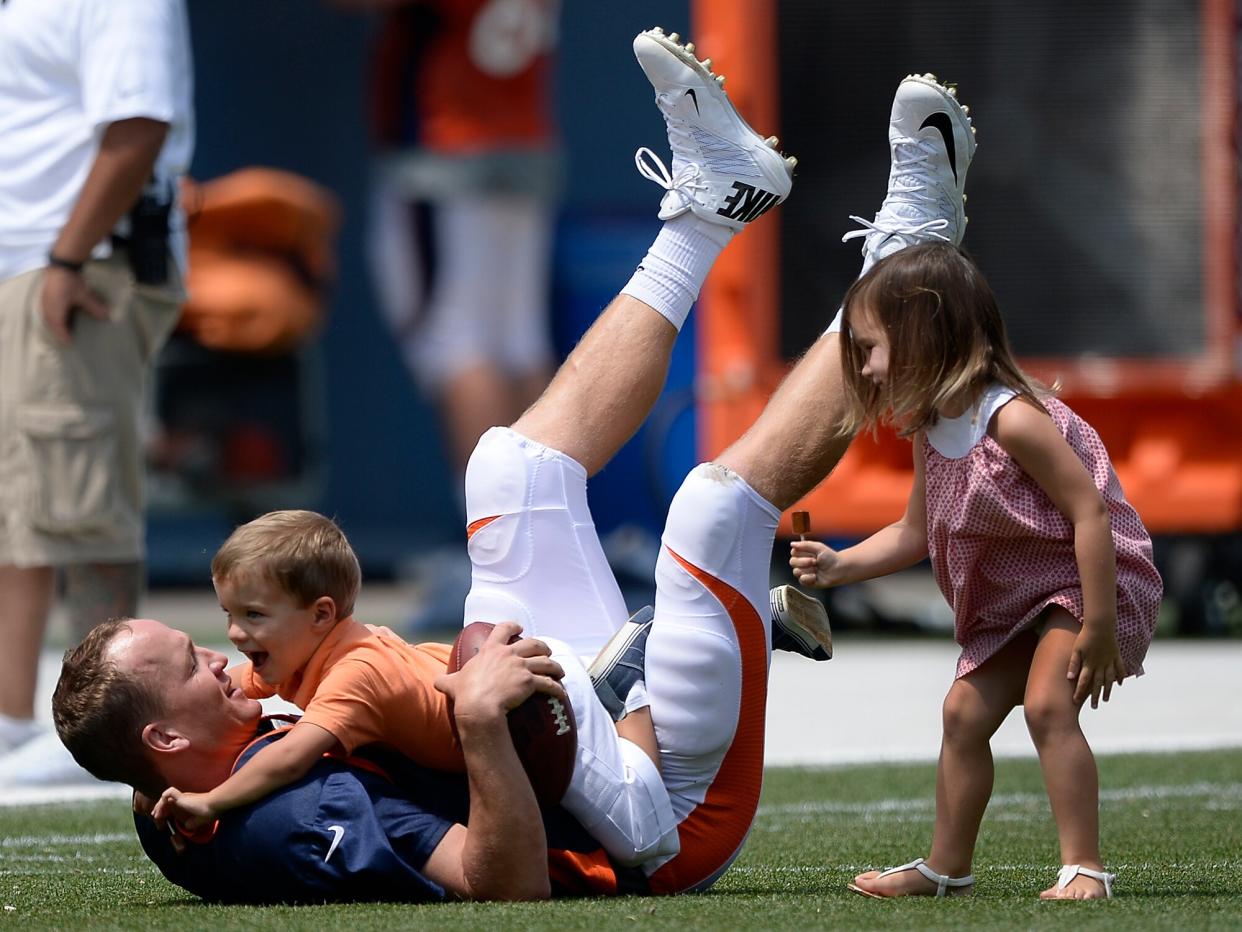 Peyton Manning (18) has a little fun with his son Marshall who tackles him and his daughter Mosley (R) after practice on day four of the Denver Broncos 2014 training camp July 27, 2014 at Sports Authority Field at Mile High
