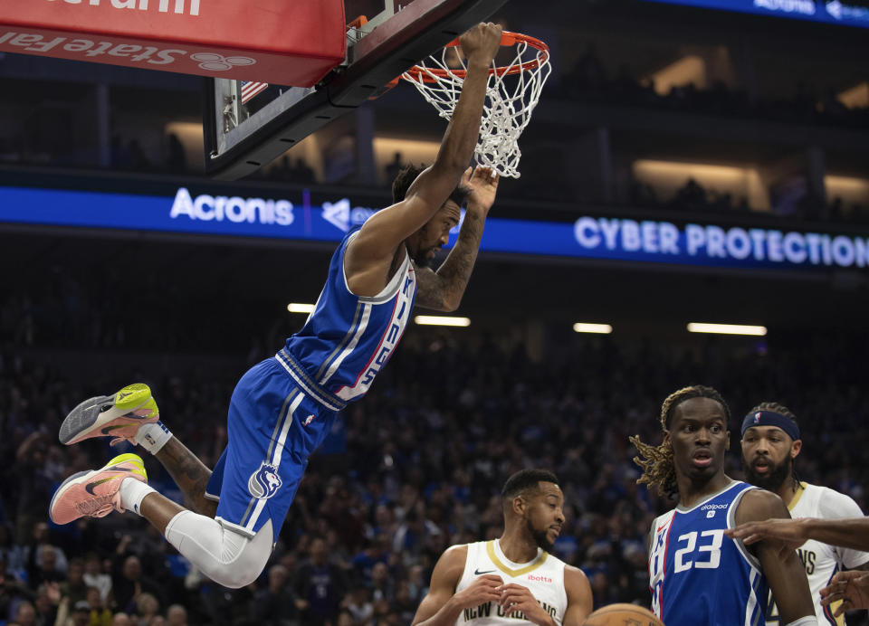 Sacramento Kings guard Malik Monk, left, hangs from the rim after scoring over Kings guard Keon Ellis (23), New Orleans Pelicans guard CJ McCollum, third from right, and Pelicans forward Brandon Ingram, right, in the first quarter of an NBA basketball game in Sacramento, Calif., Monday, Dec. 4, 2023. (AP Photo/José Luis Villegas)