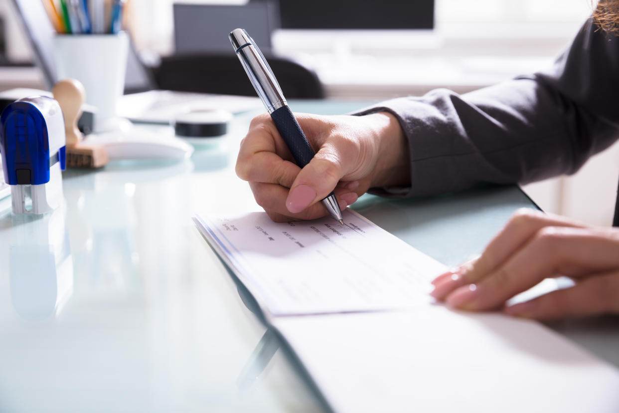 Close-up Of A Businessperson's Hand Signing Cheque With Pen In Office