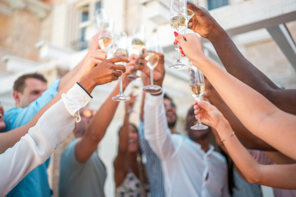 A group of people raise their champagne glasses in a celebratory toast at a wedding. Faces are not clearly visible
