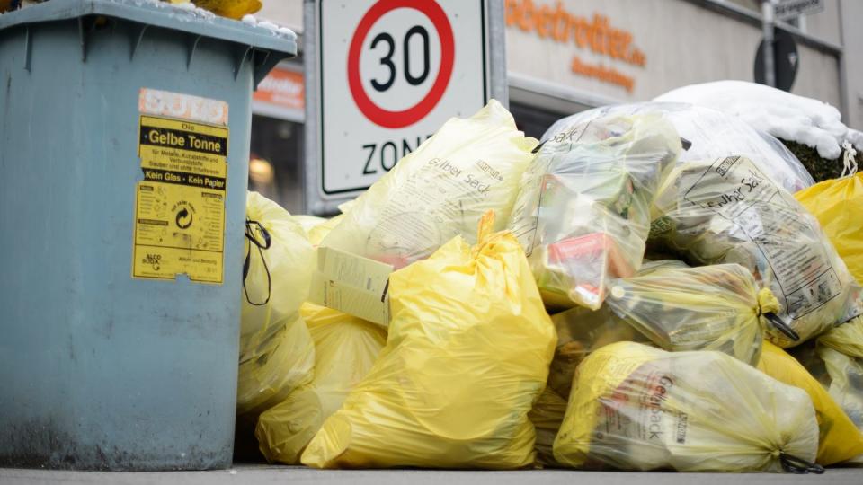 Mülltonnen und gelbe Säcke mit Kunststoff-Abfällen stapeln sich auf einem Fußweg.