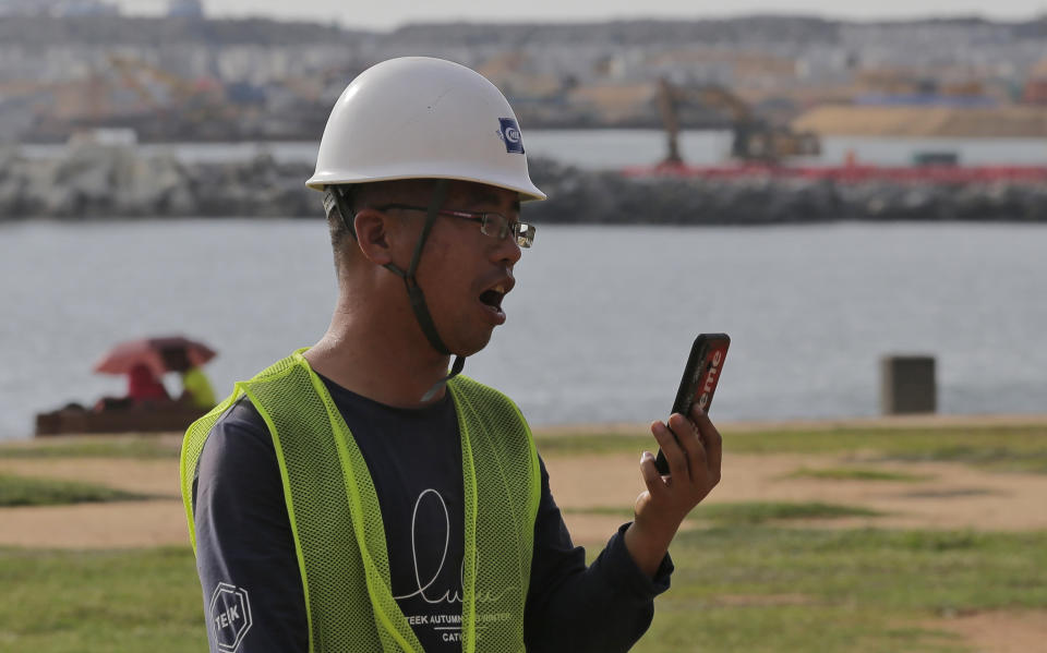 In this Saturday, Nov. 3, 2018 photo, a Chinese construction worker speaks on his mobile phone outside the Chinese funded sea reclamation project in Colombo, Sri Lanka. China and India are closely watching the constitutional crisis in Sri Lanka, the latest venue for their struggle for geopolitical supremacy in South Asia. (AP Photo/Eranga Jayawardena)