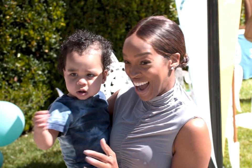 Malika smiles while holding Tatum at an outdoor event
