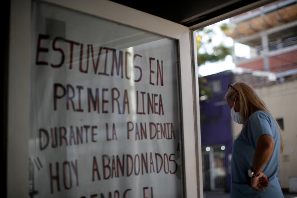 Nurse Lidia Del Valle stands by a sign that says in Spanish "We were on the front lines during the pandemic. Today, abandoned," outside San Andres Clinic which has been occupied by its former workers since it closed at the start of the year following the death of the hospital's director and owner in Caseros, Argentina, Friday, April 30, 2021. While the pandemic has swelled the need for hospital beds, many private clinics say they're struggling to survive, citing the pandemic having pushed away many non-COVID patients and losing money on coronavirus sufferers because the government insurance program doesn't pay enough to meet costs. (AP Photo/Natacha Pisarenko)