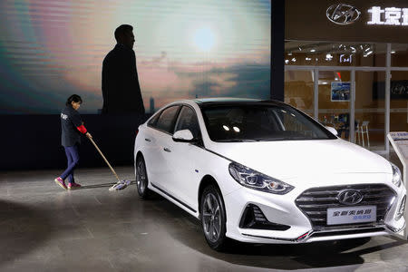 A worker cleans the floor next to a Sonata hybrid at a booth of Beijing Hyundai Motor, the joint venture between South Korea's Hyundai Motor and China's BAIC Motor, during an energy-saving and new energy vehicles expo in Beijing, China October 18, 2018. REUTERS/Thomas Peter