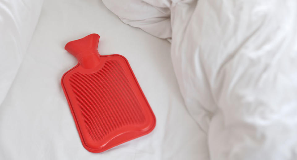 Red hot water bottle on bed with white sheets