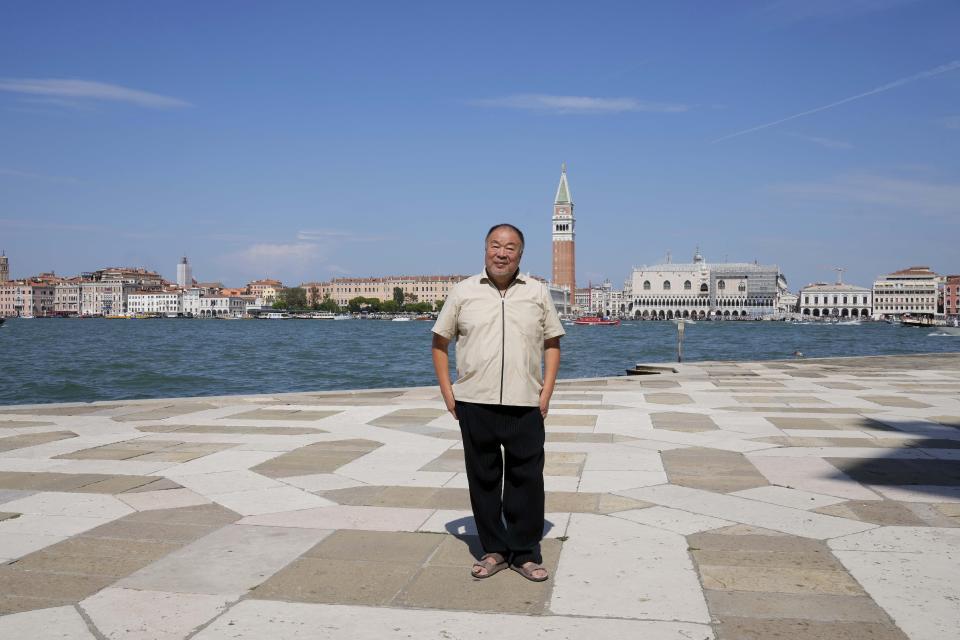 Chinese artist Ai Weiwei poses in front of Venice lagoon and San Marco's square in background, at the San Giorgio deconsecrated church in Venice, Italy, Friday, Aug. 26, 2022. Chinese artist Ai Weiwei lampoons the surveillance culture and social media with his first ever glass sculpture, made on the Venetian island of Murano, that stands as a warning to the world: "Memento Mori,'' or Latin for "Remember You Must Die." (AP Photo/Luca Bruno)