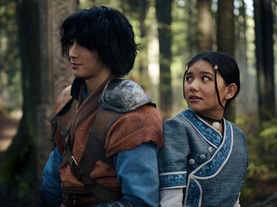 jet and katara in the avatar live action, standing back to back in a forest