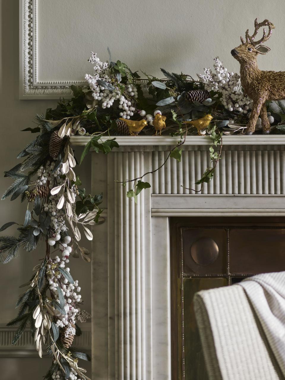 white berry style Christmas garland on mantel with three gold birds and reindeer