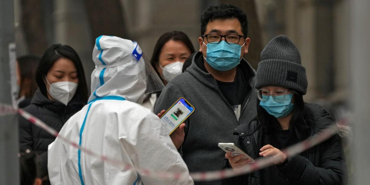 A man shows his health check QR code as he and others line up to get their routine COVID-19 throat swabs at a coronavirus testing site in Beijing, Thursday, Nov. 24, 2022.