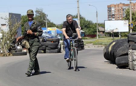 An armed pro-Russian separatist (L) stands guard at a check point as a man riding a bicycle passes by in the Ukrainian eastern city of Slaviansk July 1, 2014. REUTERS/Shamil Zhumatov