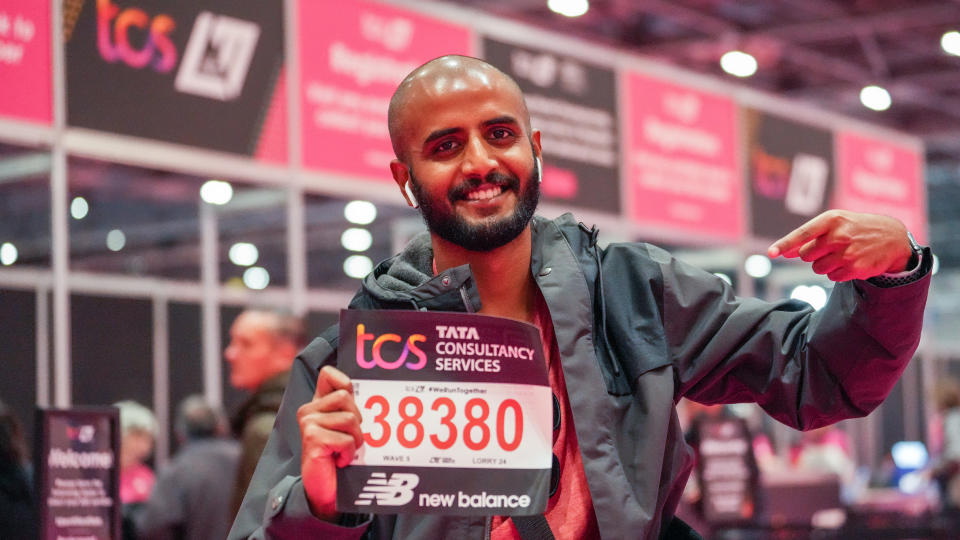  Man points at his London Marathon bib number standing in front of a row of booths at the London Marathon Running Show. 