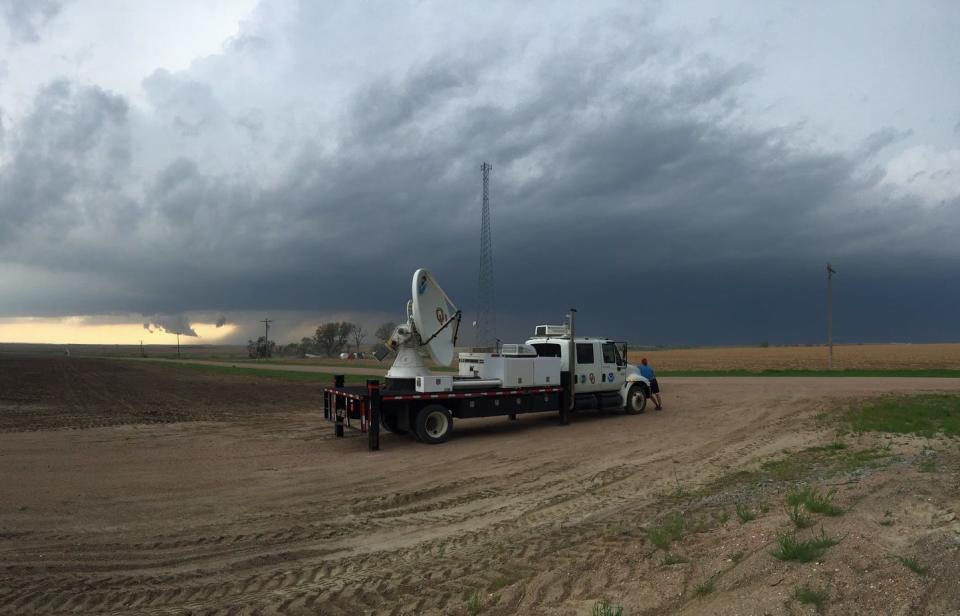 A truck with a flatbed with a large white radar dish on the back and an ominous sky in the background
