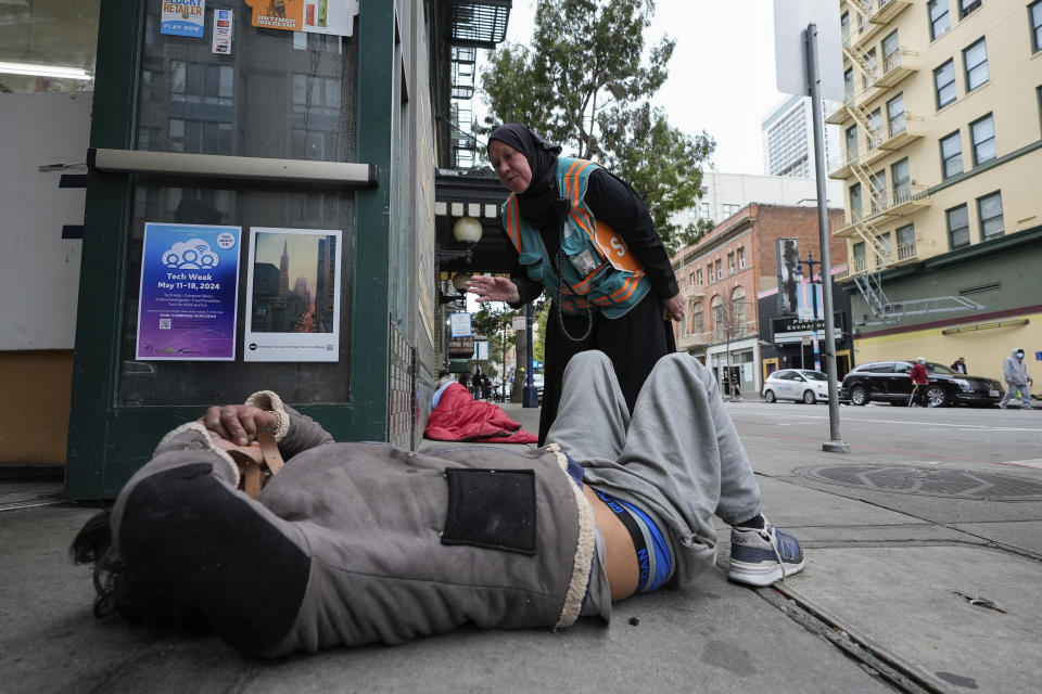 Tatiana Alabsi, right, checks on a man laying on a sidewalk and asks him to please move before children start walking to school in the Tenderloin neighborhood Wednesday, April 24, 2024, in San Francisco. (AP Photo/Godofredo A. Vásquez)