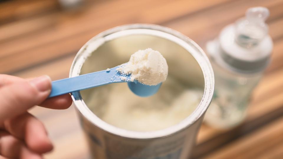 Powder milk for baby and blue spoon on light background close-up.