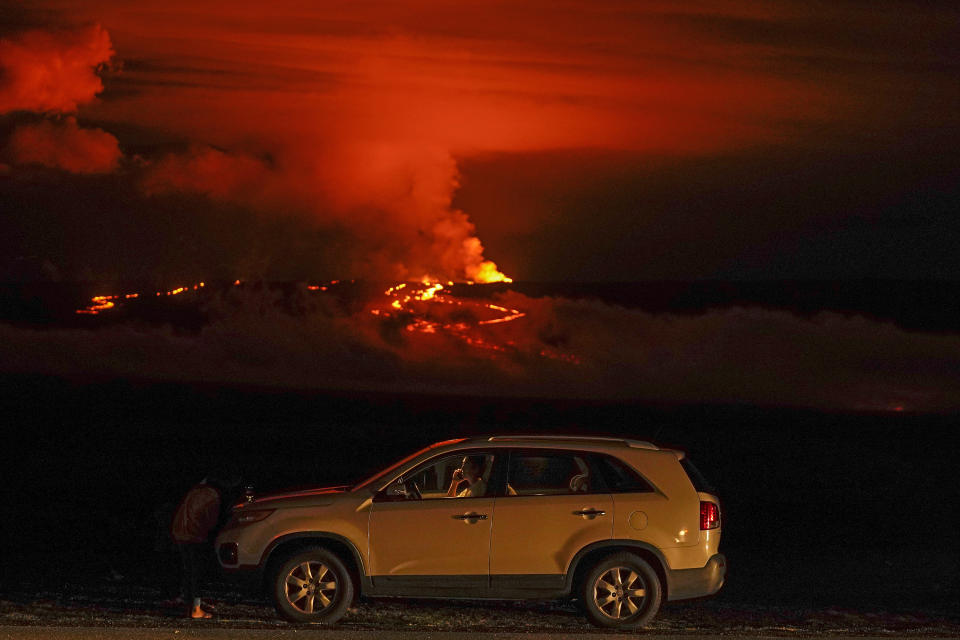 FILE - A man talks on a phone in his car alongside Saddle Road as the Mauna Loa volcano erupts Wednesday, Nov. 30, 2022, near Hilo, Hawaii. The world's largest volcano continues to erupt but scientists say lava is no longer feeding the flow front that has been creeping toward a crucial highway. That means the flow isn't advancing and is no longer an imminent threat to the road that connects the east and west sides of the Big Island. (AP Photo/Gregory Bull, File)