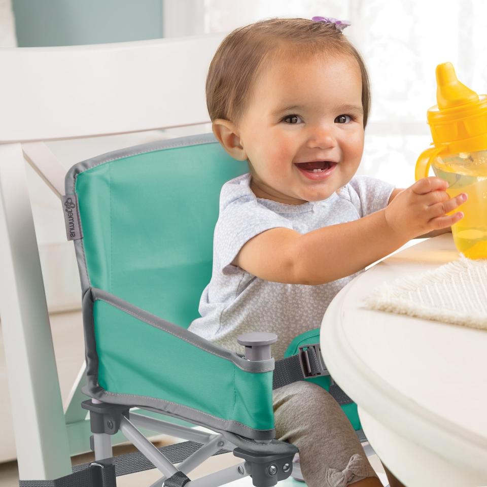 Toddler in booster seat attached to dining chair, holding a bottle