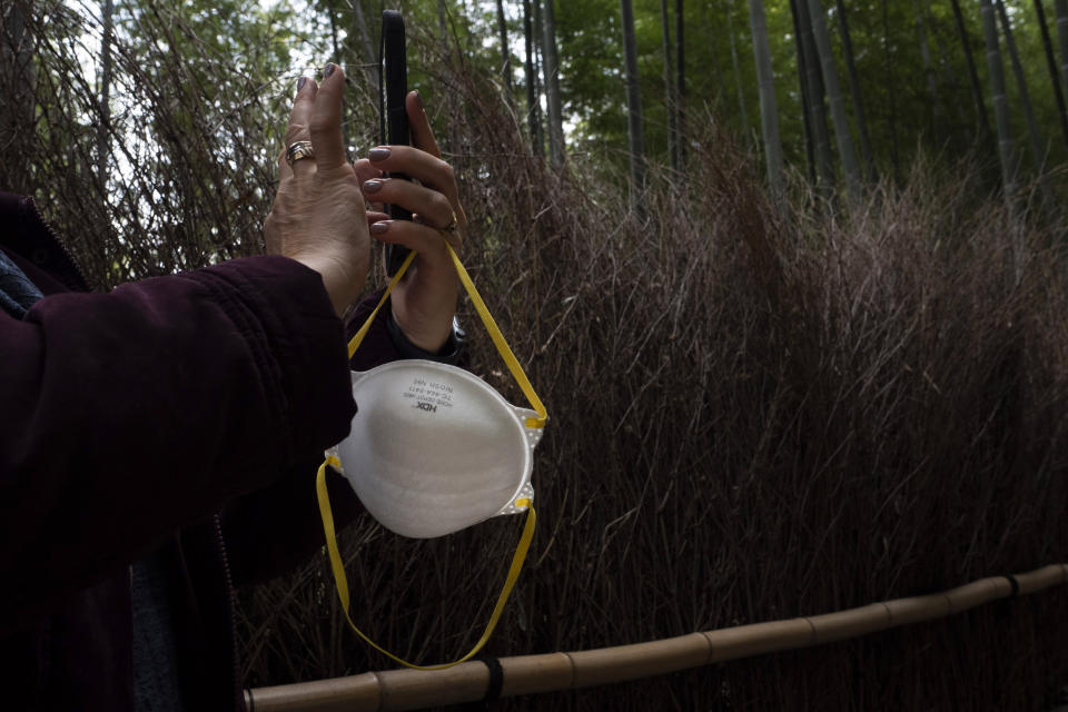 A tourist holds a mask while taking pictures of the Arashiyama Bamboo Forest in Kyoto, Japan, March 18, 2020. (AP Photo/Jae C. Hong)