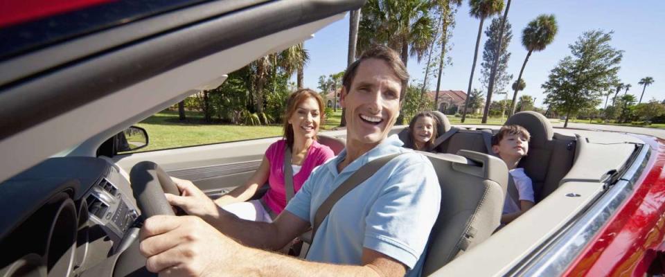 A family of four, mother, father, son and daughter driving in a convertible car on a sunny day in hot location with palm trees