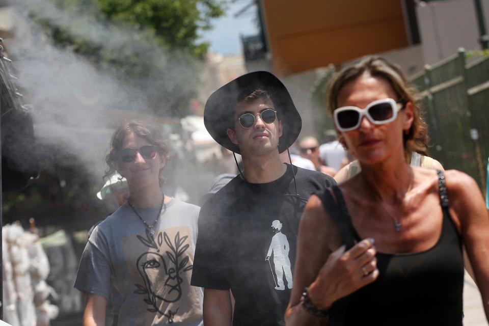 People cool off from a water spray device amid high temperatures in Athen (EPA)