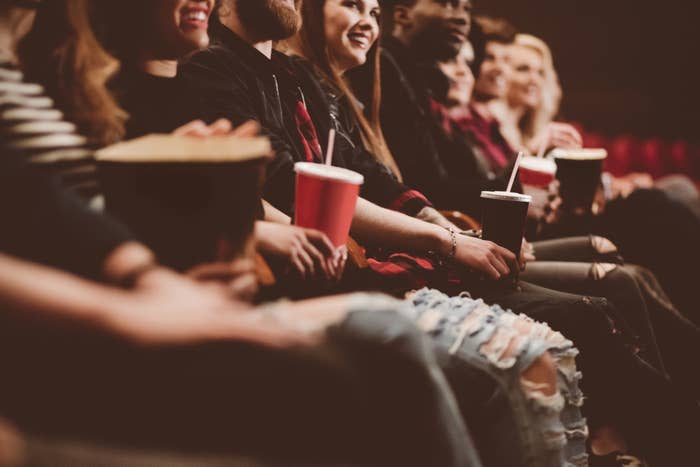 Audience members seated in a theater, holding popcorn and drinks, excitedly watching a movie