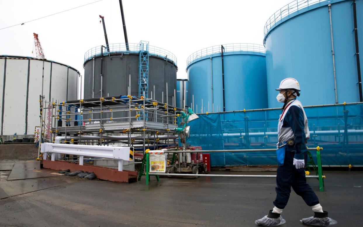 An employee walks past storage tanks for contaminated water at the tsunami-crippled Fukushima Dai-ichi nuclear power plant  - Pool Bloomberg