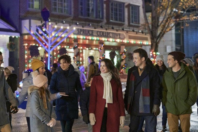 A still from the Hallmark movie "Love, Lights, Hanukkah!" A group of smiling people stand outside with a large menorah in the backround.