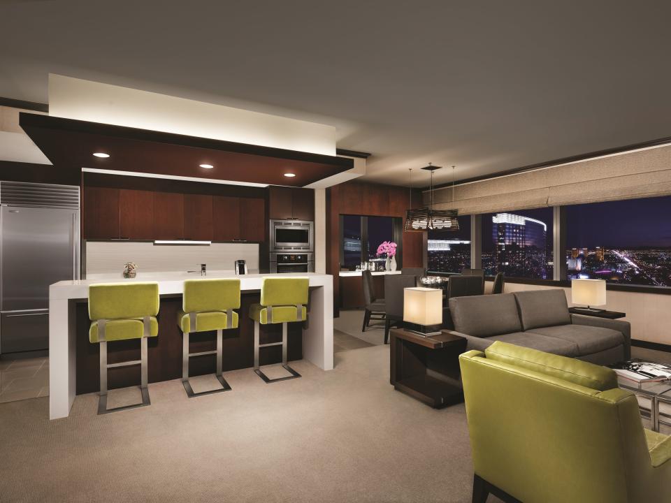 A hotel suite with a living room and kitchen we green bar seats.