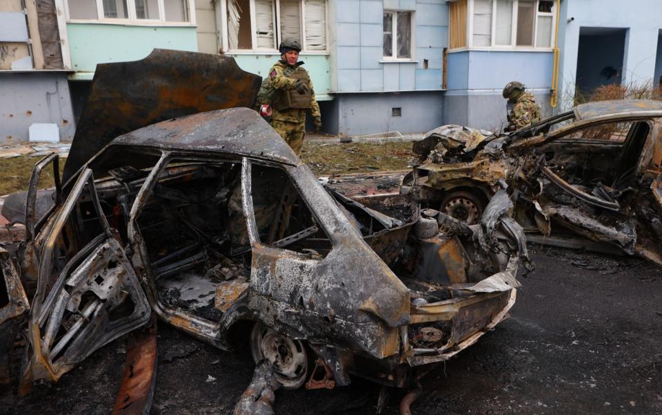 Self-defence unit volunteers stand by burned-out cars in a residential area of the city of Belgorod following fresh aerial attacks on March 22