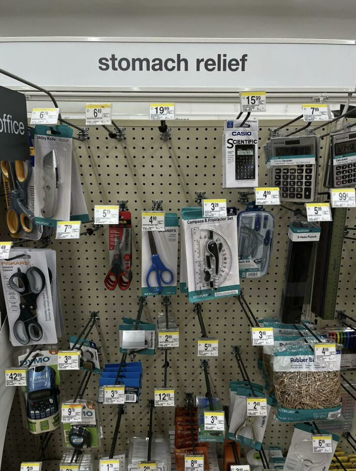 Store shelf with assorted office supplies under a "stomach relief" sign