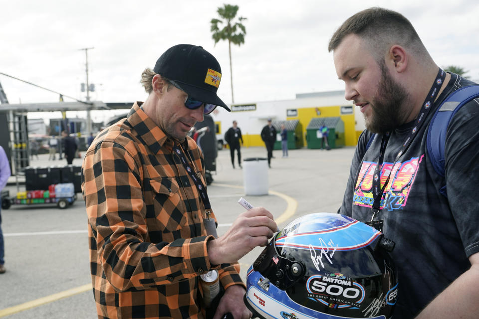 Travis Pastrana, left, autographs a helmet for a fan before a practice session for the NASCAR Daytona 500 auto race at Daytona International Speedway, Saturday, Feb. 18, 2023, in Daytona Beach, Fla. (AP Photo/John Raoux)
