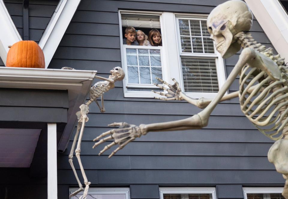 Hudson Herzig, left, with his sisters Peyton, 4, and Chloe, 11, look at the tall skeletons outside of their home in Pleasant Ridge on Tuesday, Oct. 24, 2023.