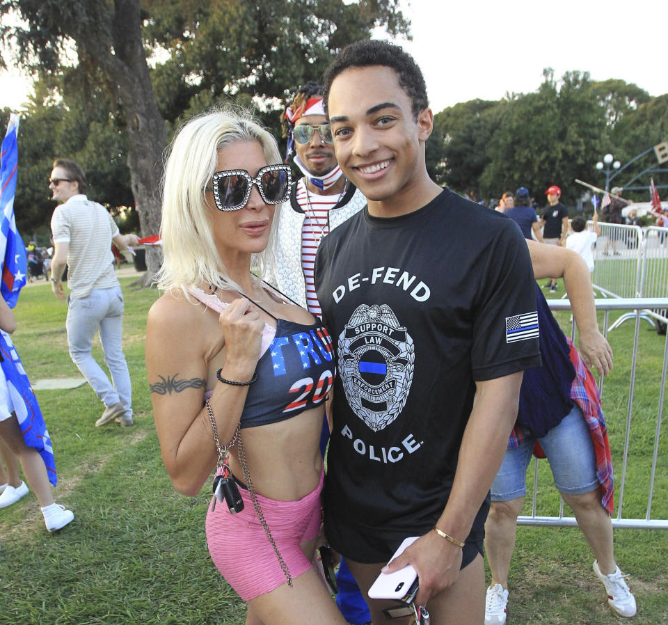 Christian Walker, his arm around a blonde woman in a bustier, pink shorts and diamond-studded sunglasses, wears a T-shirt that says: De-Fend Police, Support Law.