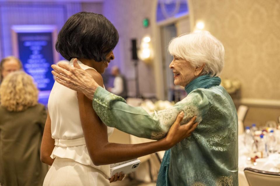 A white-haired older woman greets a young woman.