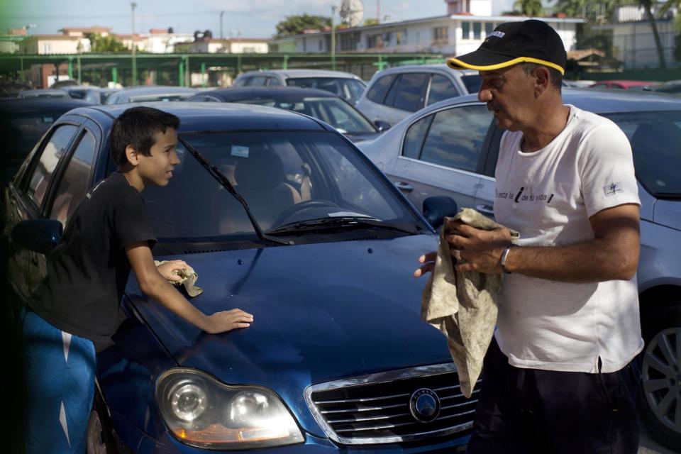 A car dealership worker, right, and a boy clean a used Chinese Geely for sale at a government-run dealership in Havana, Cuba, Thursday, Jan. 2, 2014. This car once was for sale for $5,000 dollars, but the price has risen to as much as $30,000, after a new law took effect eliminating a special permit requirement that has greatly restricted vehicle ownership in the country. (AP Photo/Ramon Espinosa)