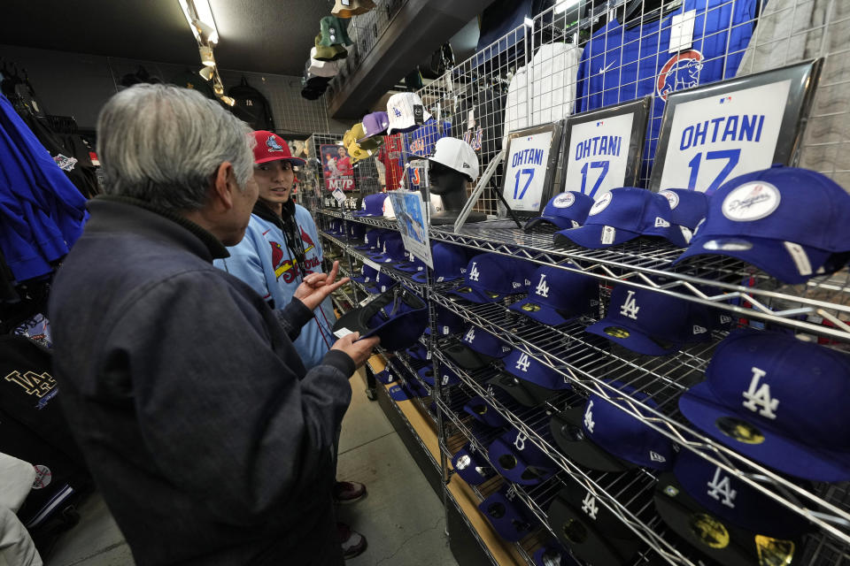 Un trabajador de la tienda le ayuda a un comprador a elegir gorras de béisbol con diferentes diseños con el nombre de Shohei Ohtani en una tienda en Tokio, Japón el 29 de febrero del 2024. (AP Foto/Hiro Komae)