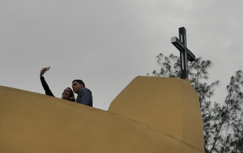 A couple pose for a photo backdropped by the cross crowning the newly consecrated Sagrado Corazon de Jesus Catholic church or Sacred Heart, in Sandino, Cuba, Saturday, Jan. 26, 2019. Of the three Catholic churches the Cuban government has authorized, it's the first one in 60 years to be completed. It was finished with the help of Tampa's St. Lawrence Catholic Church in Florida. (AP Photo/Ramon Espinosa)