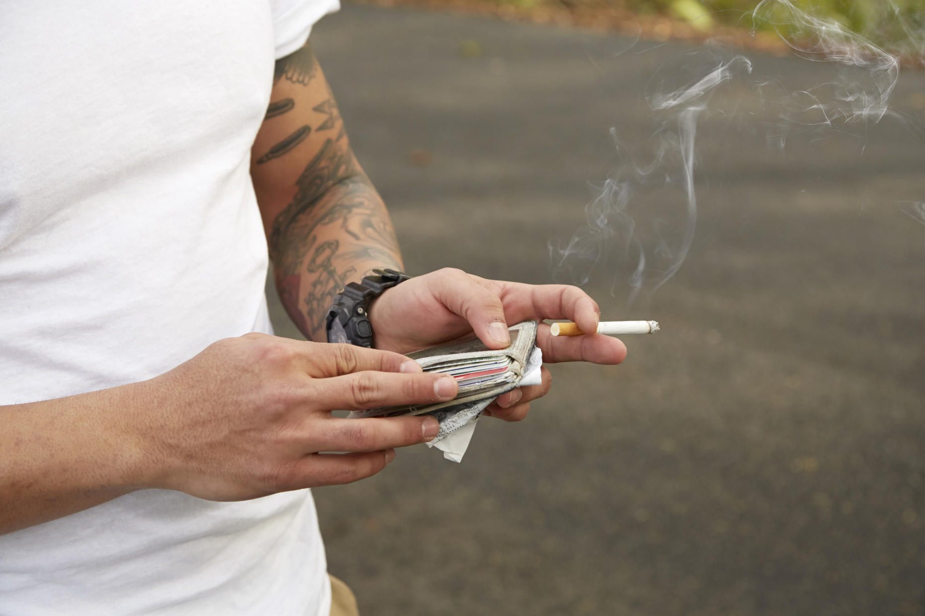 Young man holding wallet and smoking cigarette, mid section