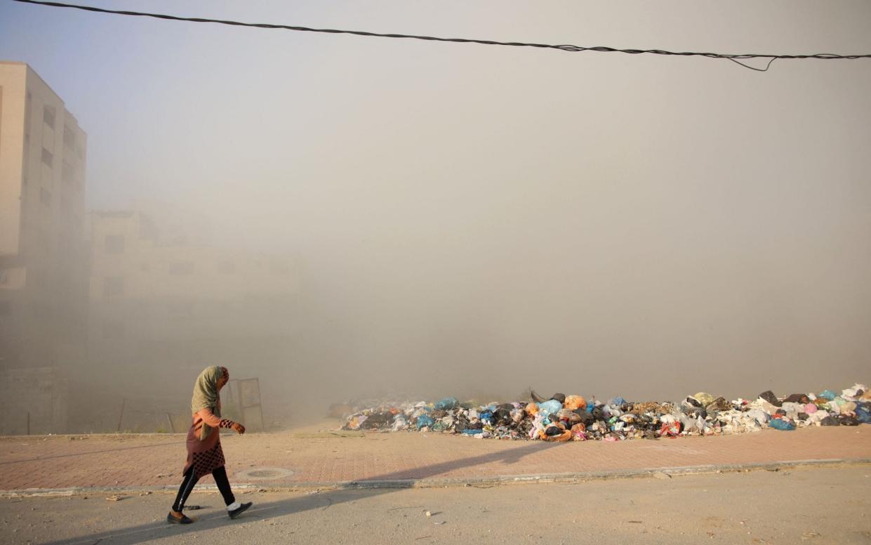 A woman walks as smoke engulfs the area after Israeli bombardment at Al-Dara