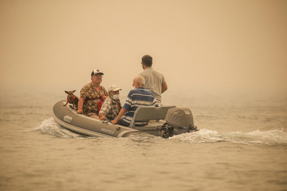 Tourists are evacuated from smoke-engulfed Mazi area as wildfires rolled down the hill toward the seashore, in Bodrum, Mugla, Turkey, Sunday, Aug. 1, 2021. More than 100 wildfires have been brought under control in Turkey, according to officials. The forestry minister tweeted that five fires are continuing in the tourist destinations of Antalya and Mugla. (AP Photo/Emre Tazegul)