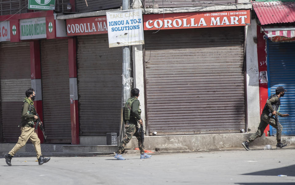 Policemen run near the site of a shootout at Sopore, 55 kilometers (34 miles) north of Srinagar, Indian controlled Kashmir, Saturday, June 12, 2021. Two civilians and two police officials were killed in an armed clash in Indian-controlled Kashmir on Saturday, police said, triggering anti-India protests who accused the police of targeting the civilians. (AP Photo/Mukhtar Khan)