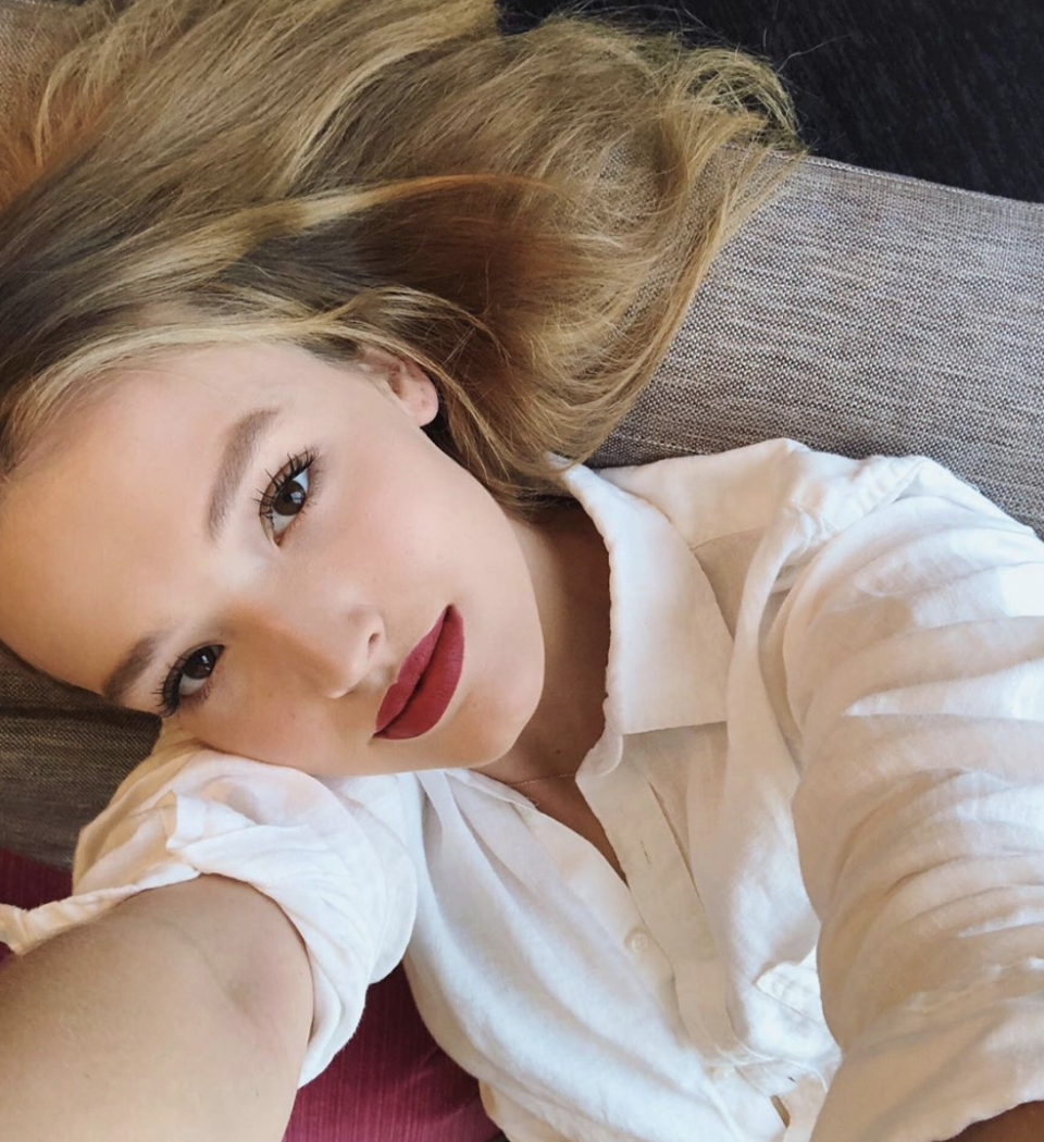 A photo of Maddison Brown wearing a white shirt and red lipstick.