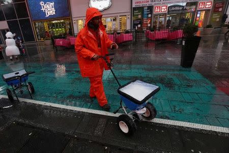 A worker spreads anti ice material as it snows in Times Square New York, New York, U.S. March 10, 2017. REUTERS/Carlo Allegri