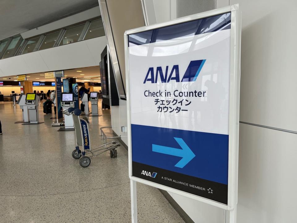 A sign in JFK Airport with a big blue arrow pointing to the right, towards the ANA check-in counter.