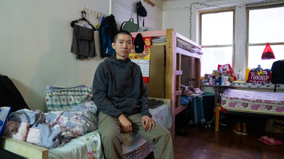 Li Jiada sits on his bed in a room he shares with five other men in Flushing, Queens. - Yong Xiong/CNN