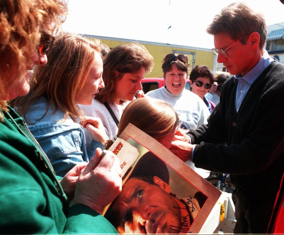 In this 1995 photo, Harrison Ford signs autographs outside his dressing room for adorning fans in Vineyard Haven during the filming of the movie "Sabrina" which was being shot Martha's Vineyard.