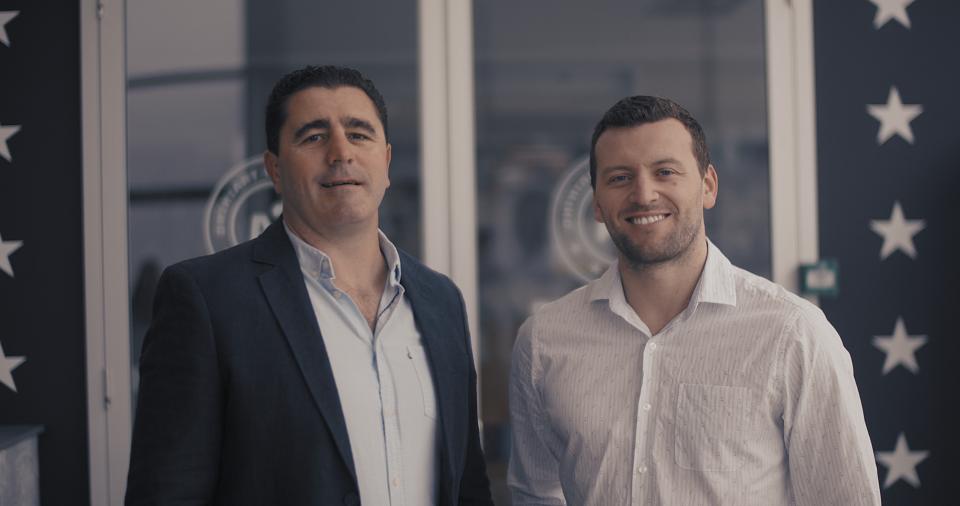 Two male entrepreneurs standing together smiling in front of their gym business